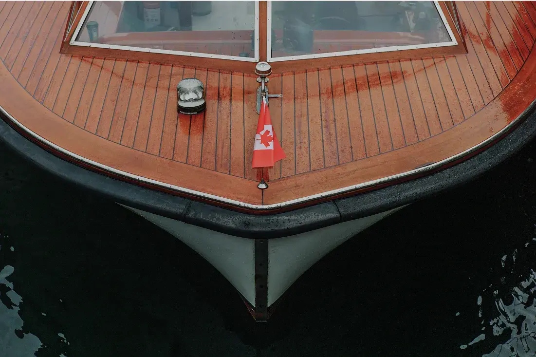 Close-up of a wooden boat deck with a small Canadian flag at the bow, docked on dark water.